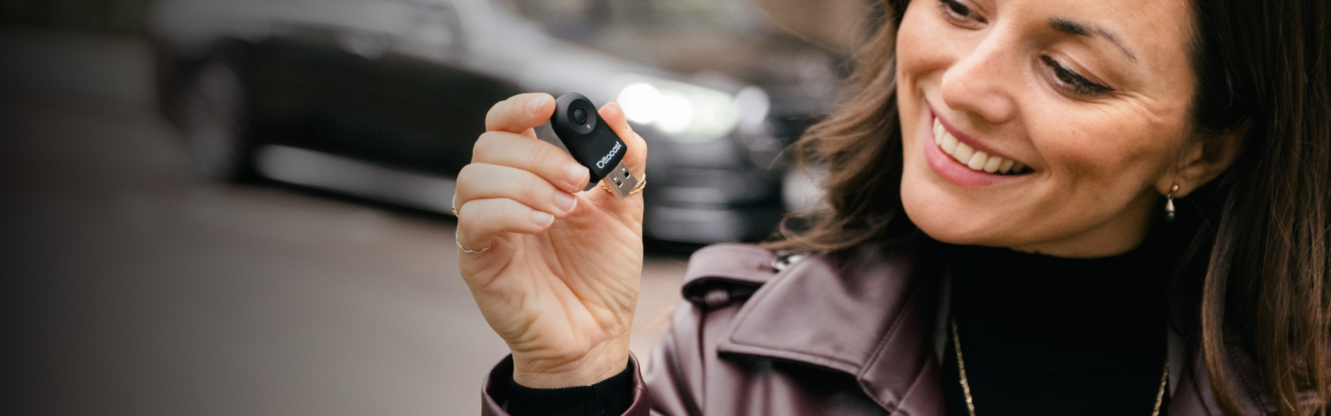 Smiling woman holding Ottocast mini USB device for wireless CarPlay and Android Auto connection