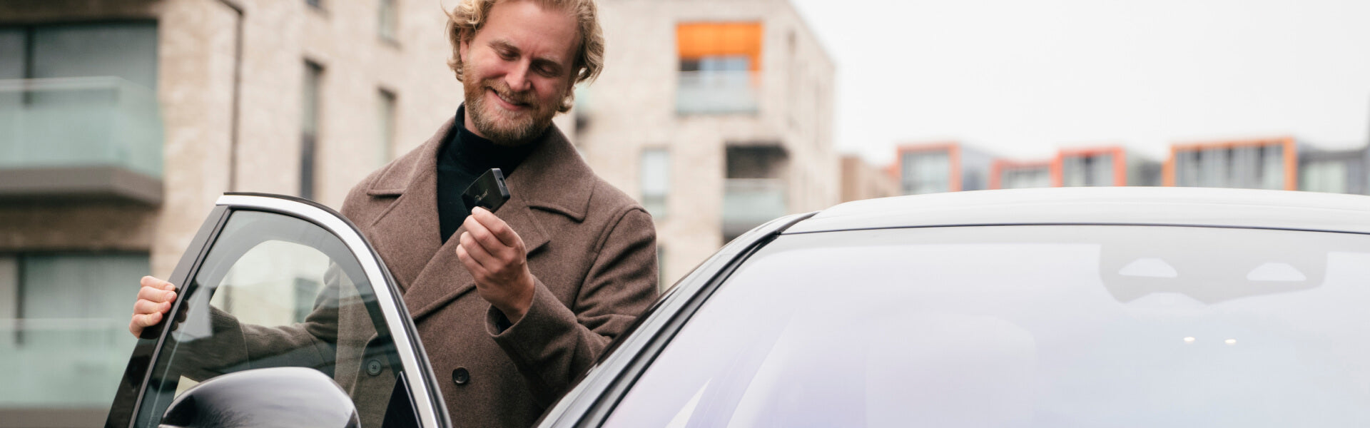 Man holding Ottocast Play2Video Pro wireless CarPlay and Android Auto adapter beside car for seamless in-car connectivity